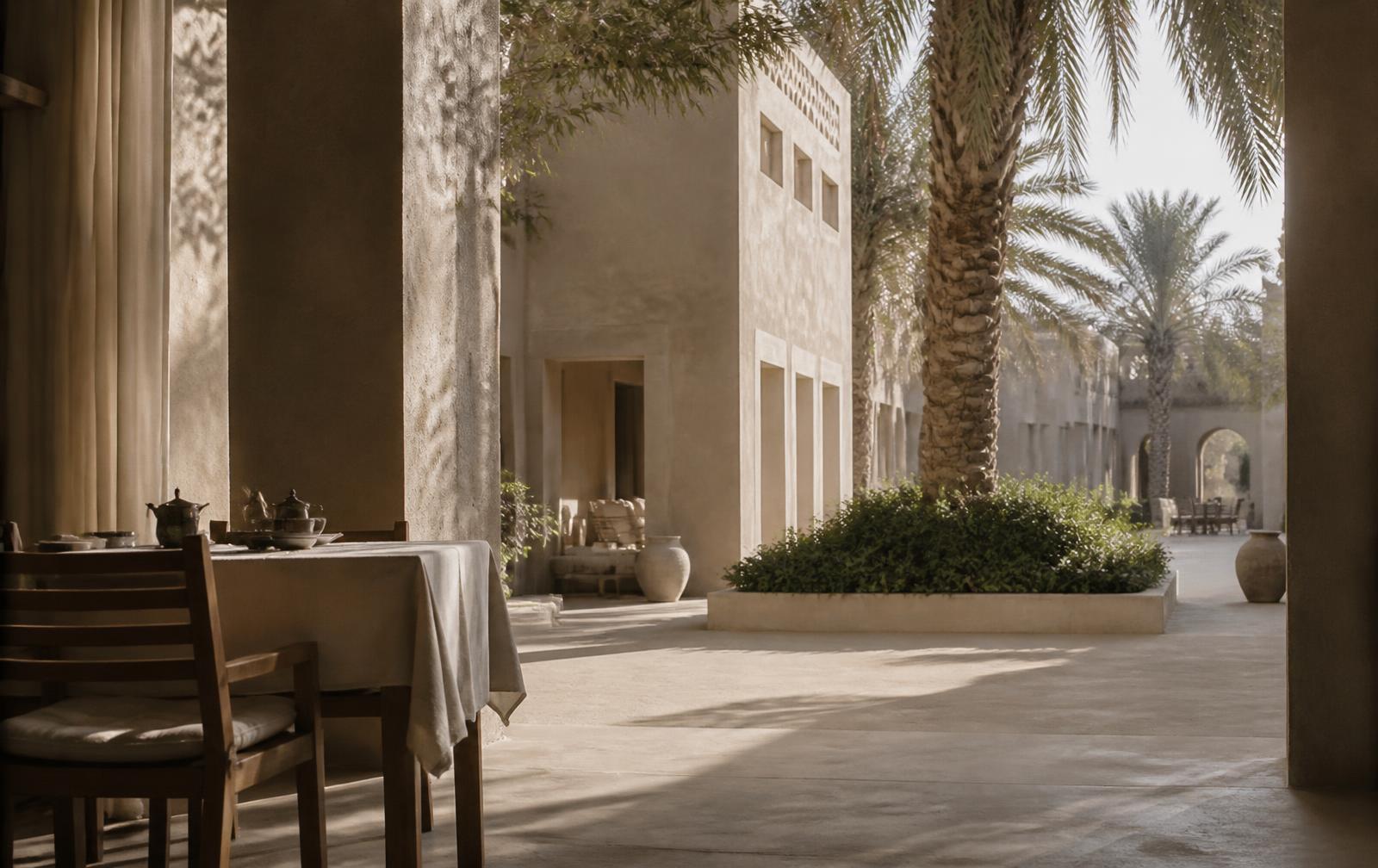Quiet hotel courtyard in early morning light with palm shadows across stone and linen