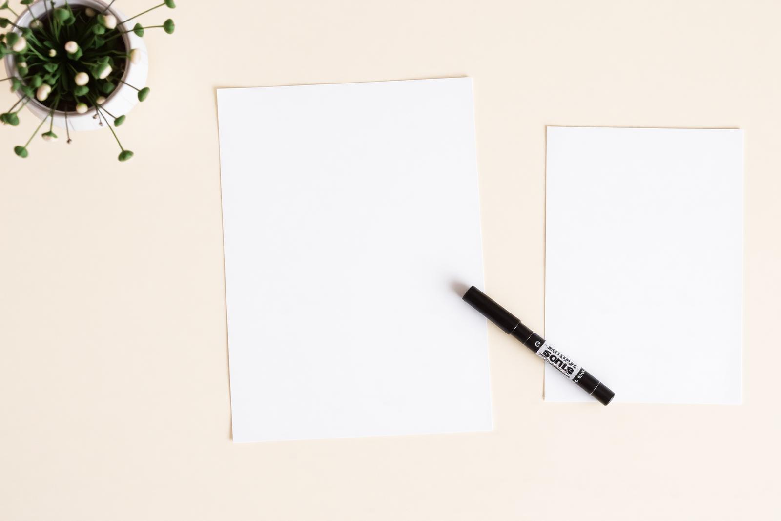 Blank poster prints and card crops laid out with a marker on a warm off-white desk